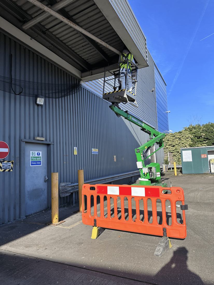A painter on a lift working on tall industrial cladding
