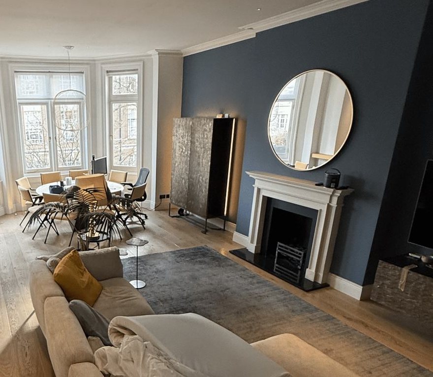 A navy chimney wall behind a white fireplace, in a room with a bay window