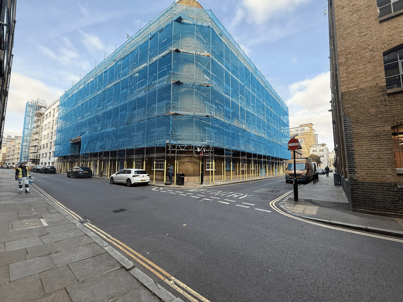 A large brick building wrapped in blue scaffold sheeting on a London street
