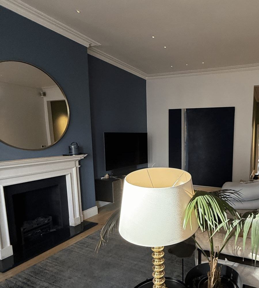 A navy chimney wall above a white fireplace, with a round mirror