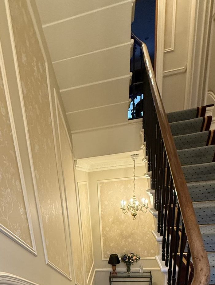 A panelled stairwell with a timber handrail and a chandelier